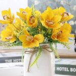 Cette image montre une fausse fleur jaune. Cette fleur artificielle est une orchidée. Cette fausse fleur est dans un vase