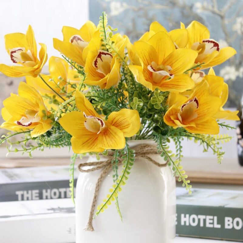 Cette image montre une fausse fleur jaune. Cette fleur artificielle est une orchidée. Cette fausse fleur est dans un vase