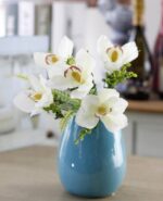 Cette image montre une fausse fleur blanche. Cette fleur artificielle est une orchidée. Cette fausse fleur est dans un vase