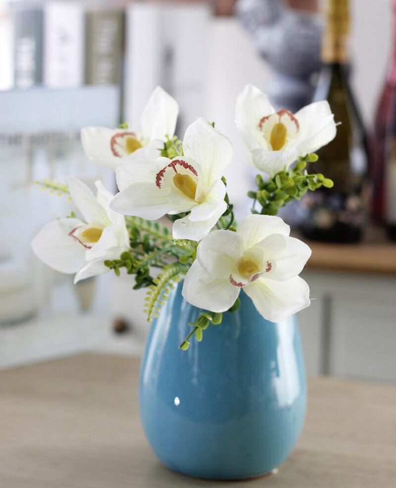 Cette image montre une fausse fleur blanche. Cette fleur artificielle est une orchidée. Cette fausse fleur est dans un vase
