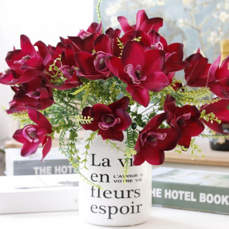 Cette image montre une fausse fleur rouge. Cette fleur artificielle est une orchidée. Cette fausse fleur est dans un vase